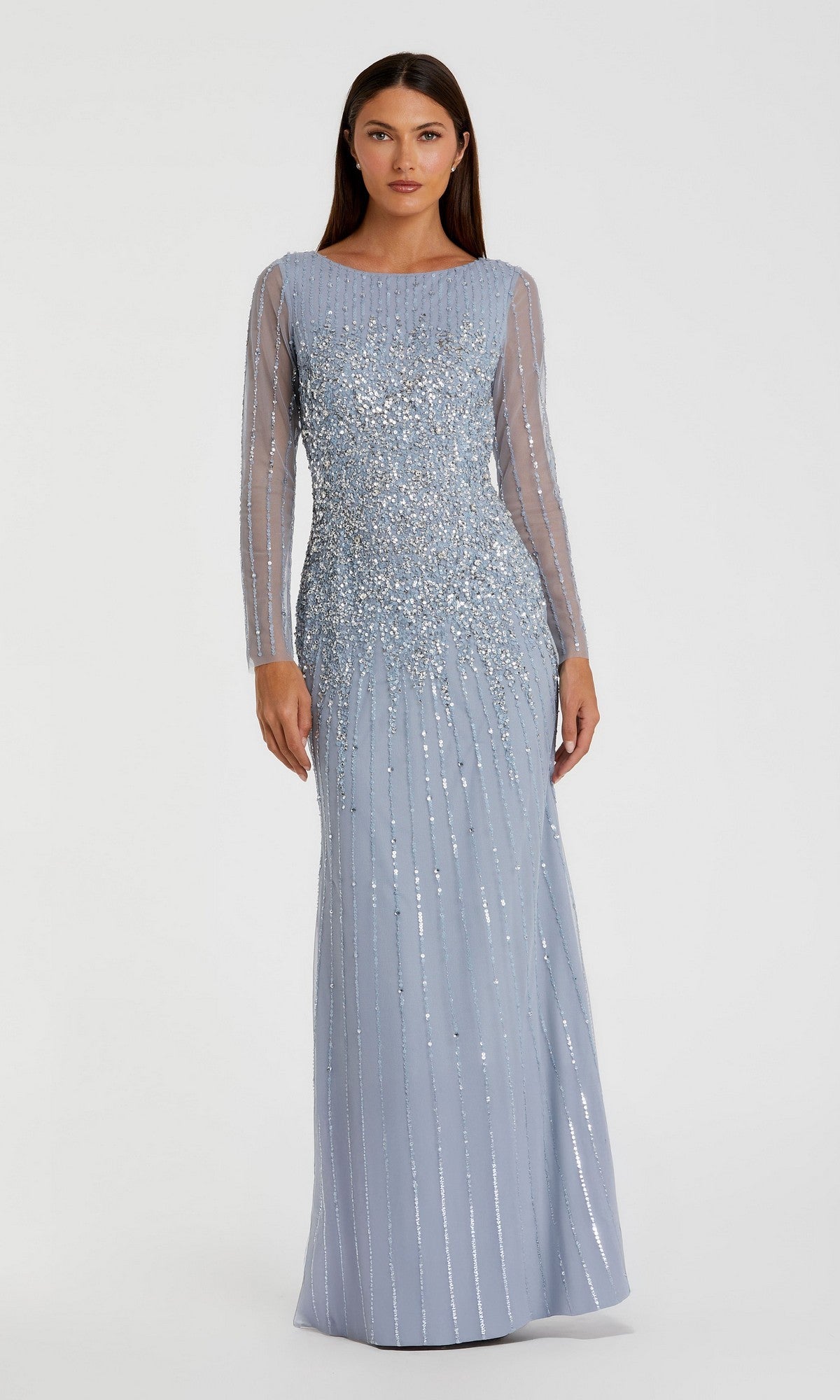A woman wears the Mac Duggal 9226 Long Sleeve Sequin Formal Gown, featuring sheer long sleeves, as she stands facing forward against a plain background.